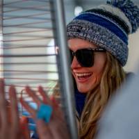 An alum wearing a winter hat warms up her hands at a heater